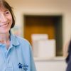 A smiling woman in a blue Guide Dogs tee looks past the camera. 