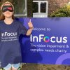 Photo is of an 11 year old girl, wearing a blind fold, standing in front of InFocus Charity Logo