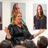 Woman making a speech in front of a series of portrait photographs depicting Everyday Bravery
