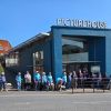 A group of volunteers with their guide dog pups in training stand in front of the Exeter Picturehous