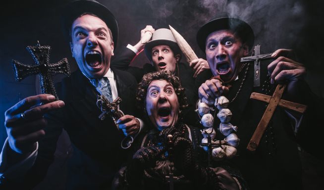 Le Navet Bete stand in a group holding garlic and crucifixes with a look of farcical fear on their faces. 