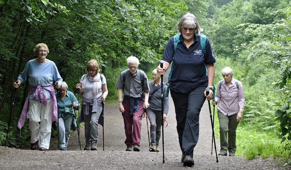 Six over 50s are following a Nordic walking leader up a hill