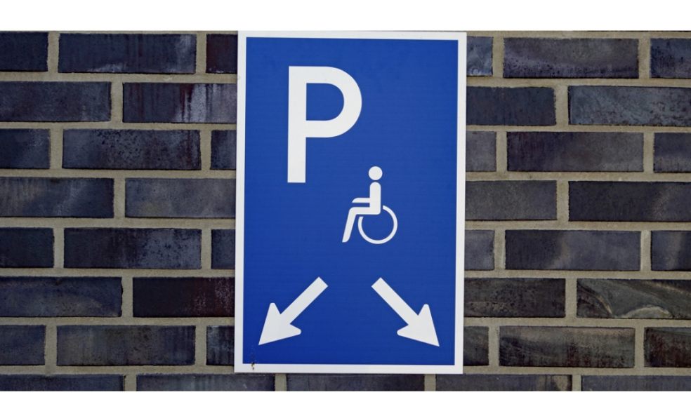 Disabled parking sign pointing at parking spaces on a grey brick wall