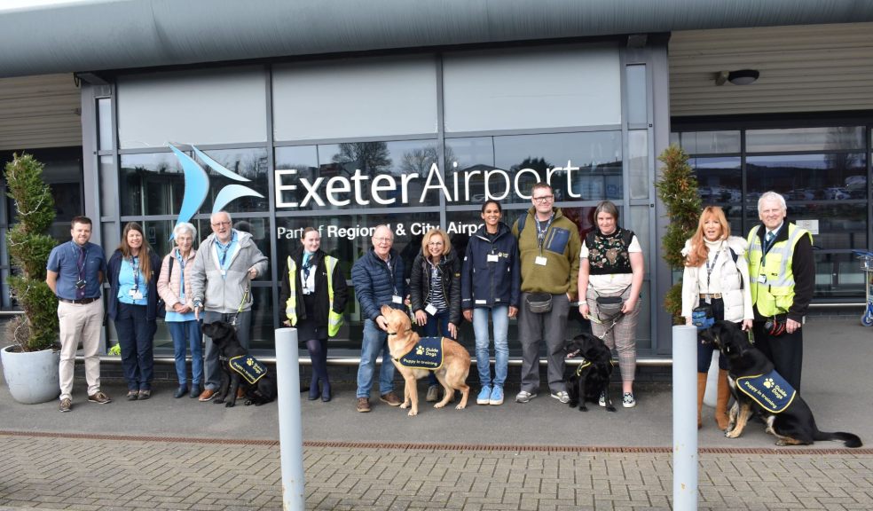 Staff, volunteers and puppies stand in front of the airport building.