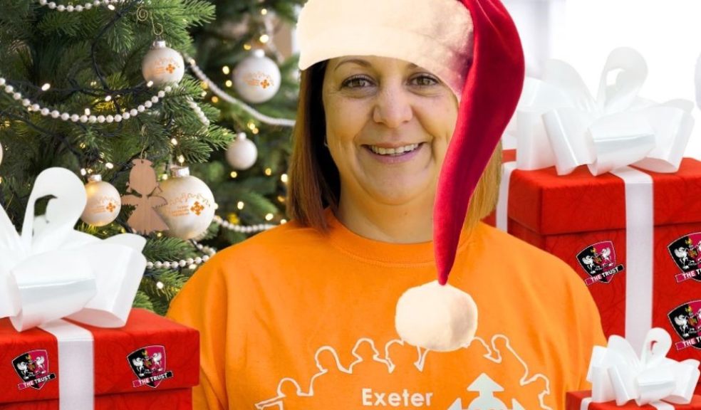 woman wearing Santa hat and orange T-shirt with gifts standing in front of a Christmas tree