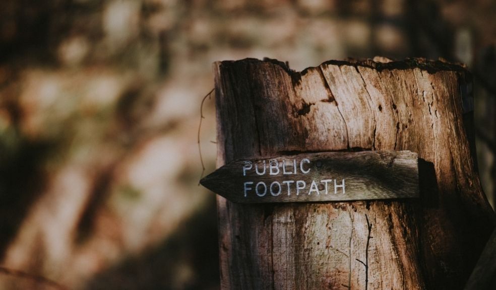 A photograph of a public footpath sign on a treestump, with woodland behind