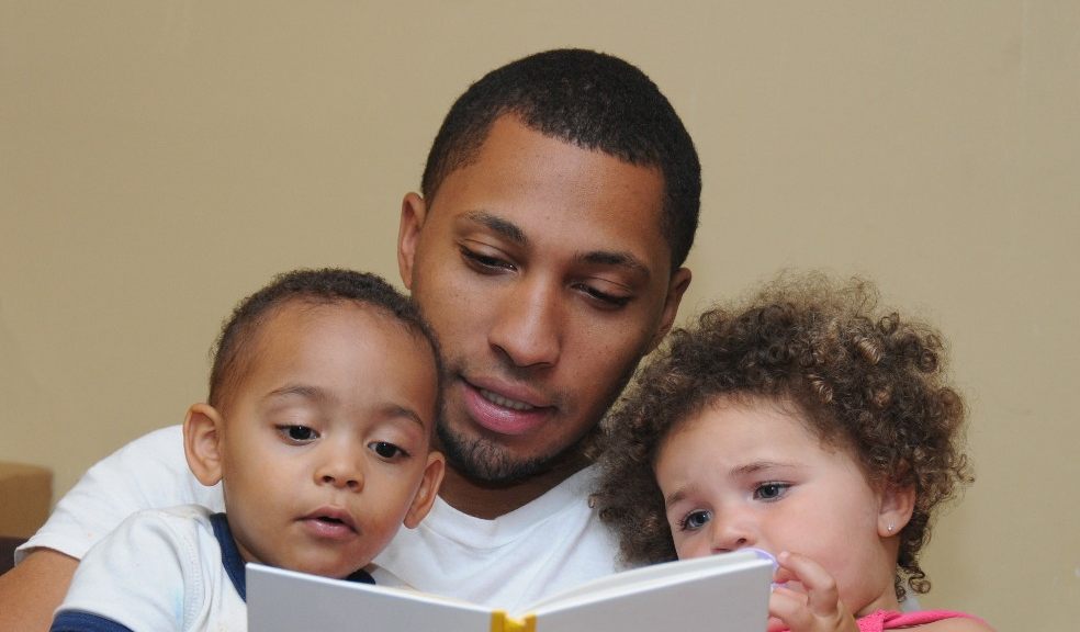 Photograph showing a man reading a book to two children Photograph showing a man reading a book to two children