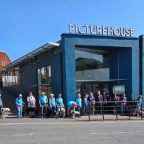 A group of volunteers with their guide dog pups in training stand in front of the Exeter Picturehous