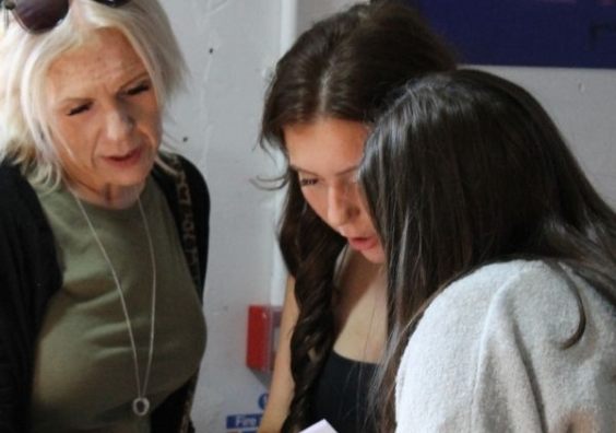 Queen Elizabeth's School GCSE Results Day Three people gather indoors, reviewing exam results; an older woman leans beside two young women.