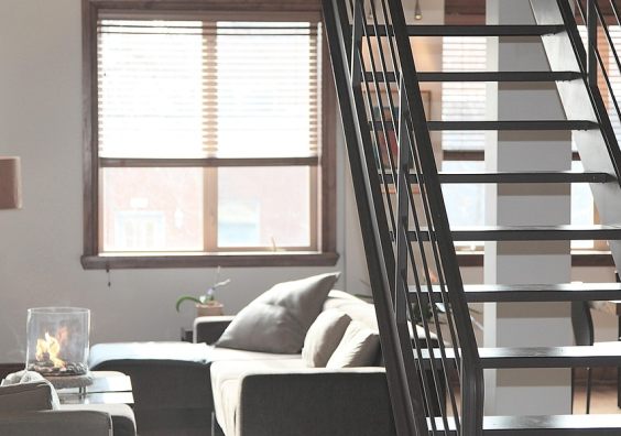 sunlit modern loft living room with grey sofas, windows, metal staircase and a small table top fire