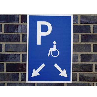 Disabled parking sign pointing at parking spaces on a grey brick wall