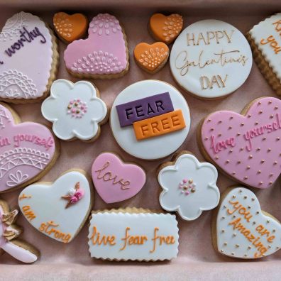 Purple, orange and white heart shaped and flower shaped cookies with empowering messages iced  on