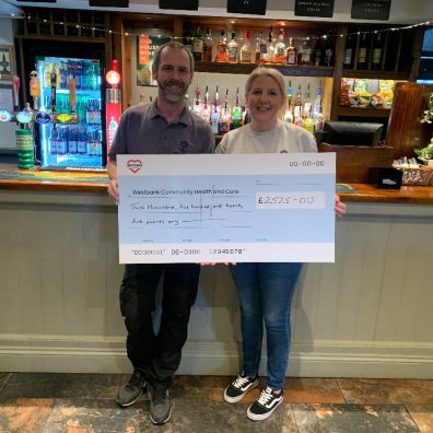 photo of man and woman holding a fundraising cheque in front of a pub bar