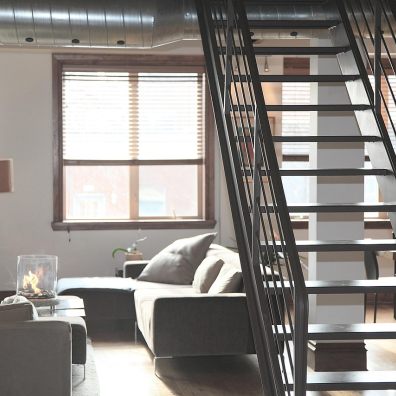 sunlit modern loft living room with grey sofas, windows, metal staircase and a small table top fire